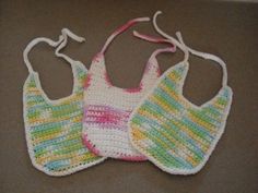 three crocheted bibs are hanging on a wall together, one is white and the other is multicolored