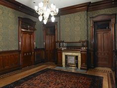 an empty room with wood paneling and chandelier hanging from the ceiling in front of a fireplace