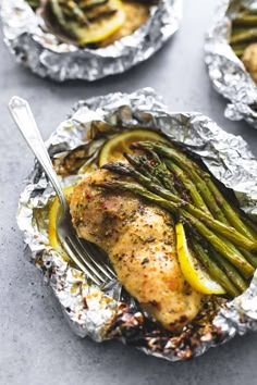 chicken and asparagus wrapped in tin foil on a plate with a fork next to it