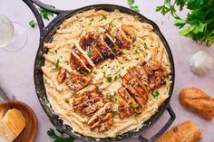 a skillet filled with pasta and chicken on top of a white table next to bread