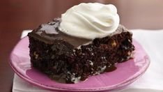 a piece of chocolate cake with whipped cream on top sits on a pink paper plate