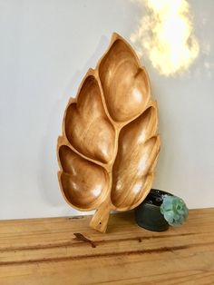 a wooden bowl sitting on top of a wooden table next to a green flower vase