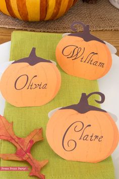 three pumpkin place cards sitting on top of a green napkin next to a white plate