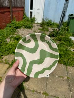 a hand holding a green and white paper plate in front of a brick building with grass growing around it