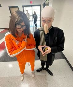 two people in costumes standing next to each other on a hallway with an orange and white striped wall