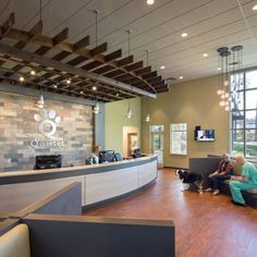 two people sitting on couches in front of a reception desk with a dog standing next to them