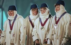 four women in white robes with medals on their heads