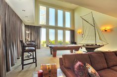 a living room filled with furniture and a pool table in front of two large windows