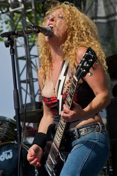 a woman singing into a microphone while holding a guitar in front of her face and on stage