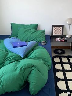 an unmade bed with green comforter and blue pillow on the floor next to a black table