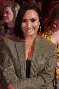 a woman sitting in a chair with her arms crossed and smiling at the camera while other people look on