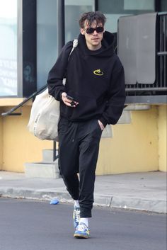 a man walking down the street wearing sunglasses and a black sweatshirt with a yellow smiley face on it