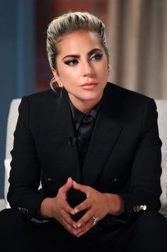 a woman in a black suit sitting on top of a white chair with her hands crossed