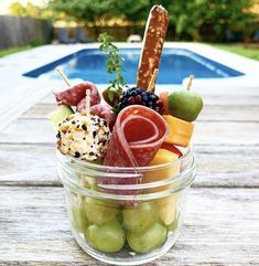 a glass bowl filled with assorted fruits and meats next to a swimming pool