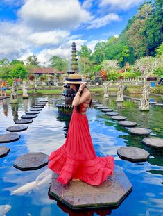 a woman in a red dress is standing on stepping stones and looking at the water