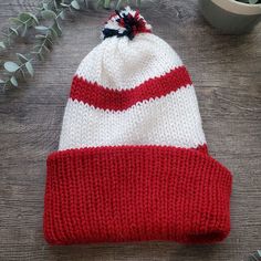 a red and white knitted hat sitting on top of a wooden table next to a potted plant