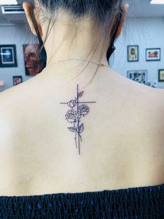 a woman's back neck with a cross and flowers tattoo on her left shoulder