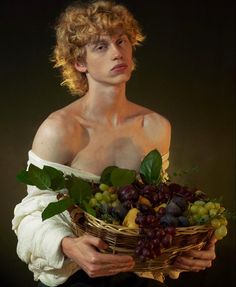 a man with curly hair holding a basket full of grapes and other fruit in his hands