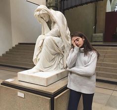 a woman standing in front of a statue talking on a cell phone while holding her hand up to her ear