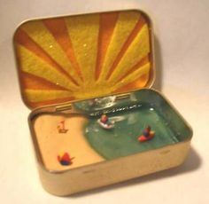 an open tin box with miniature people on the beach in water and sunbursts