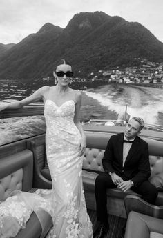 a man and woman in formal wear on a boat with mountains in the background, black and white photo