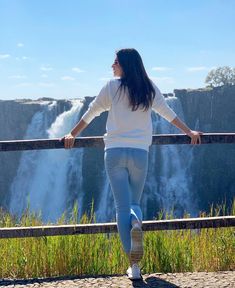 a woman is standing at the edge of a cliff overlooking a waterfall and looking into the distance