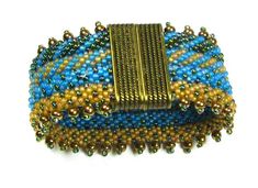 a blue, yellow and brown beaded brooch on a white background with beads