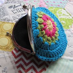 a crocheted coin purse sitting on top of a quilted tablecloth with a metal hook