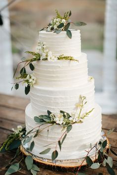 a white wedding cake with flowers and greenery on top sitting on a wooden table