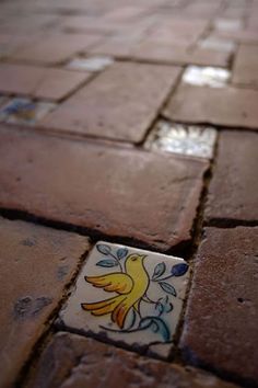 a close up of a tile floor with a yellow bird painted on the side and small square tiles