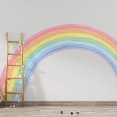 a ladder leaning against a wall with a rainbow painted on the wall in front of it