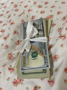 one hundred dollar bills tied with a white ribbon on top of a bed covered in pink flowers