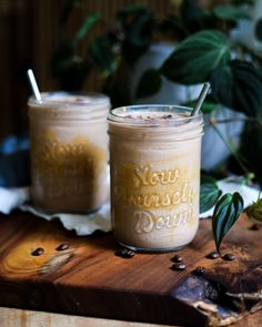 two mason jars filled with iced coffee sit on a wooden table next to green plants