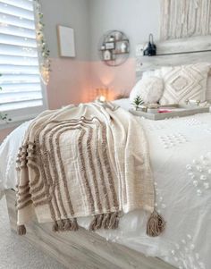 a bed with white linens and fringed blankets on it, next to a window