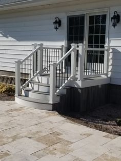 a white house with steps leading up to the front door and side porch area that has stone pavers on both sides