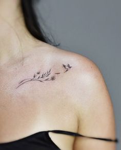 the back of a woman's shoulder with small tattoos on her left shoulder and two flowers