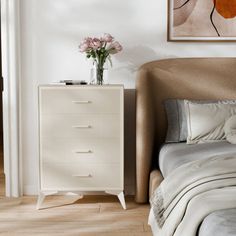 a white bed sitting next to a dresser with flowers on it