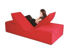 a woman sitting on top of a red couch that is shaped like an arrow and has her legs crossed