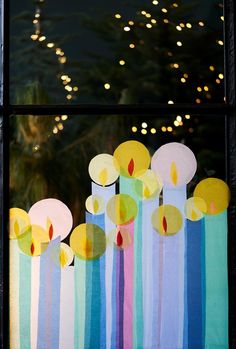 candles are lit in front of a window decorated with colored paper and lights behind them