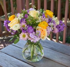 a vase filled with lots of colorful flowers on top of a wooden table next to a fence