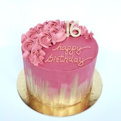 a pink and gold birthday cake with flowers on it's top, sitting on a plate