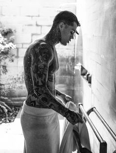 a man with tattoos standing next to a stair case