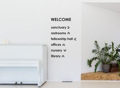 there is a welcome sign on the wall next to a white piano and potted plants