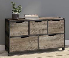 a wooden dresser with four drawers and a potted plant on top, against a gray wall