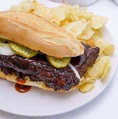 a steak sandwich with pickles and onions on a plate next to potato chips