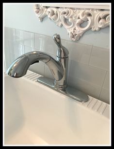 a faucet in a bathroom sink next to a white tile wall and mirror