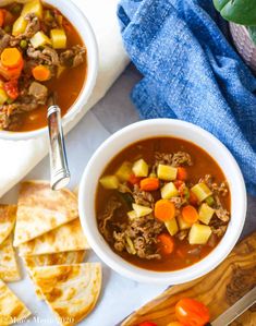 two bowls of beef and vegetable soup with tortilla crackers on the side