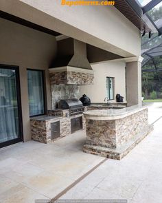 an outdoor kitchen with stone counter tops and grills on the outside wall, surrounded by glass doors