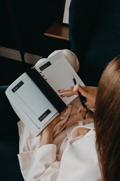 a person sitting on a couch with a book and pen in their hand while writing