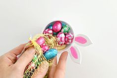 a person holding a bowl filled with chocolate eggs and bunny ears on top of it